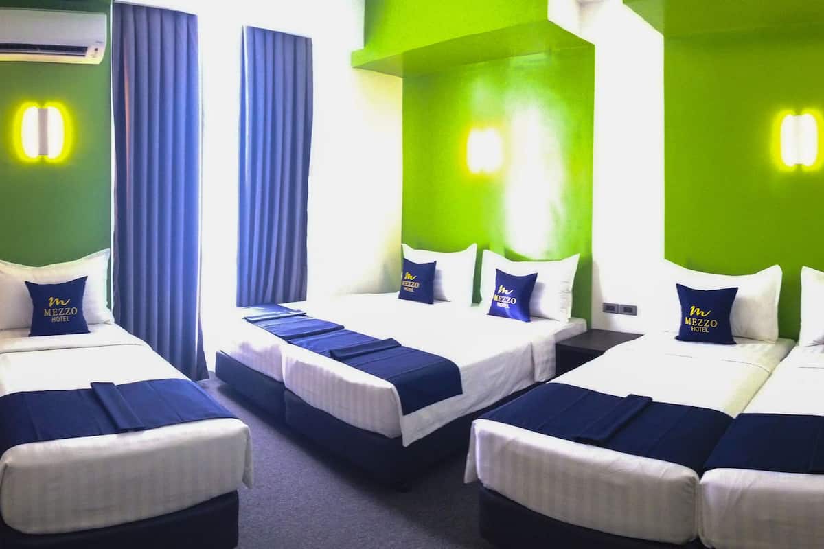 Quarto de hotel com quatro camas dispostas em forma de U, cada uma com uma almofada exibindo o logotipo do hotel.