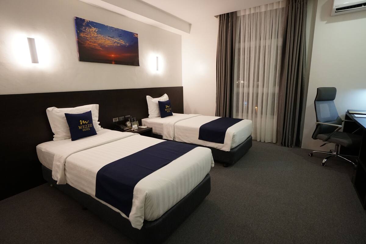 Quarto de hotel com duas camas, uma escrivaninha e uma cadeira.