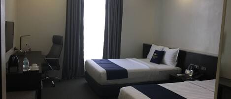 Habitación de hotel con dos camas, un escritorio con una silla, una lámpara de escritorio, una botella de agua, una taza y un minibar.