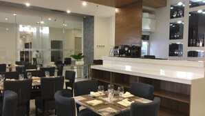 Un restaurant moderne avec des chaises sombres, une table surmontée d’un plateau en marbre et une machine à café.
