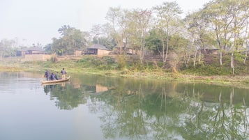 Un río tranquilo con una pequeña embarcación que transporta a tres personas. Edificios bordean la orilla del río, rodeados de árboles.