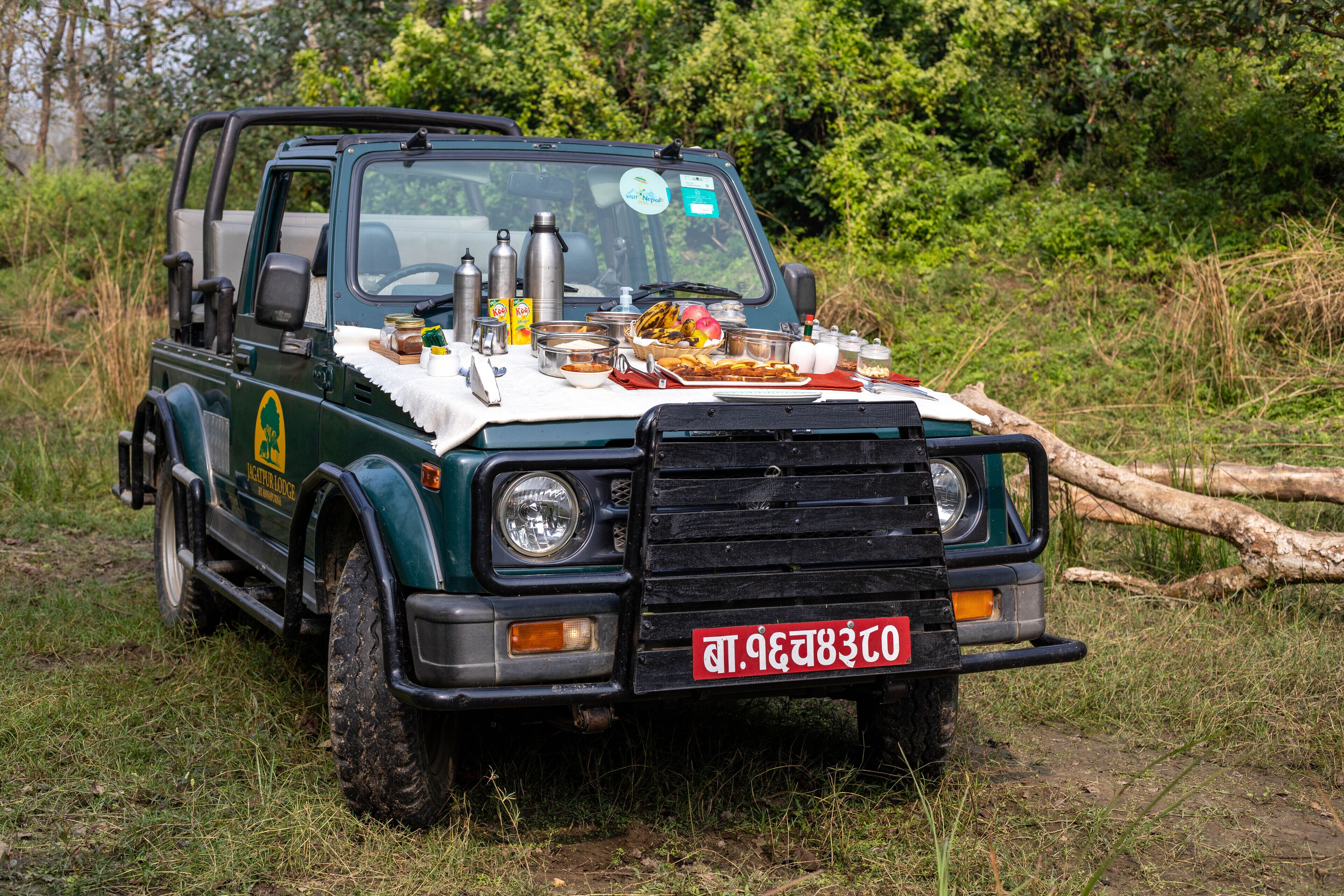 A green safari vehicle with a table loaded with food and drinks in the front.