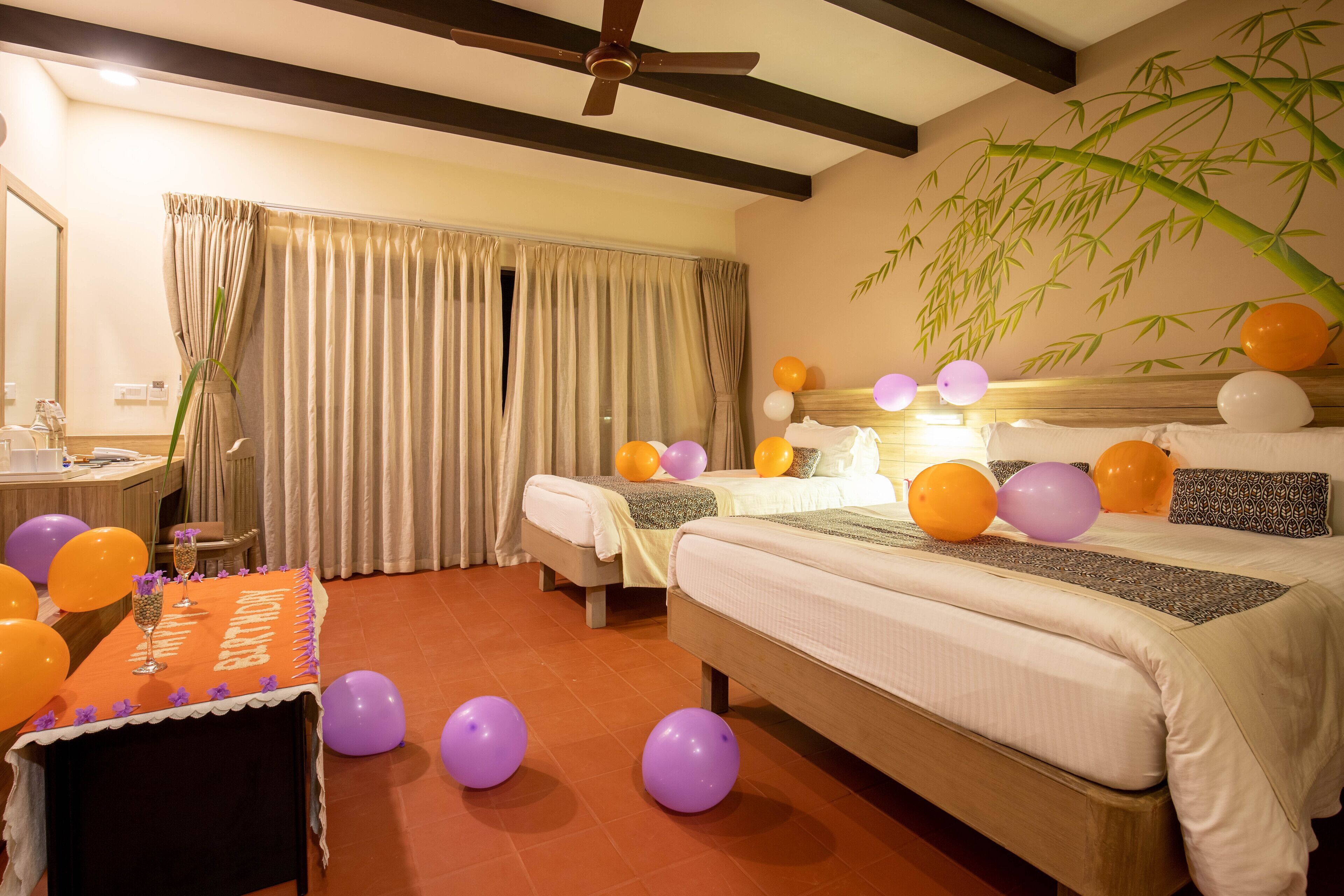 Una habitación de hotel con una cama, una mesa con globos y un ventilador de techo.