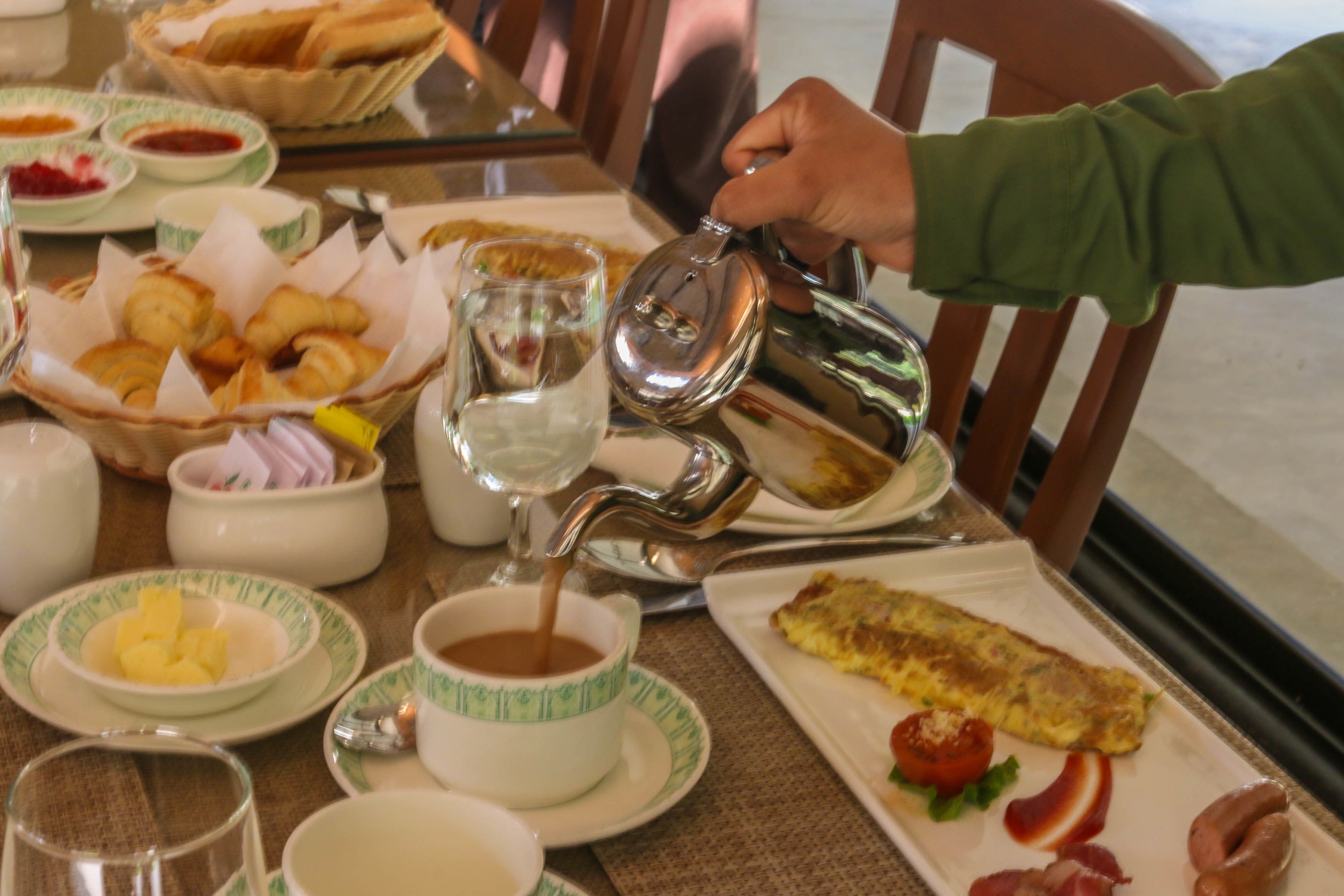 Desayuno con cruasanes, una bebida caliente siendo servida y un plato con tortilla y tomate.