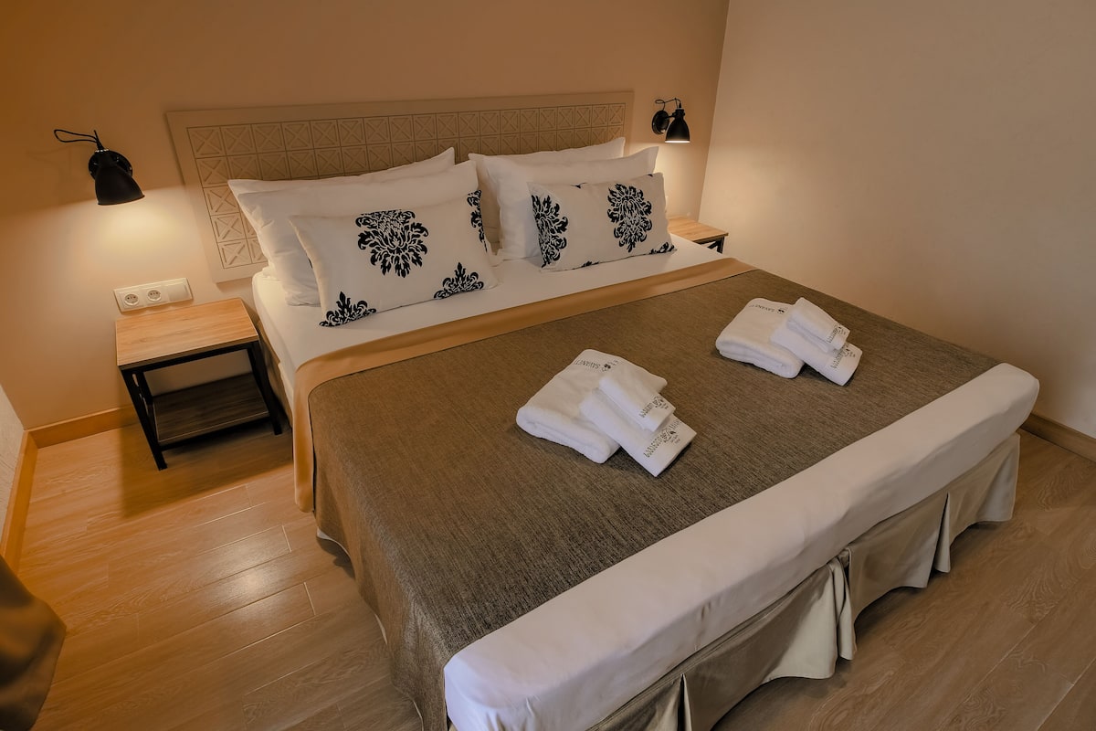 Cama bem arrumada com almofadas estampadas em branco e preto, um espalha-mau e duas toalhas dobradas sobre a cama.