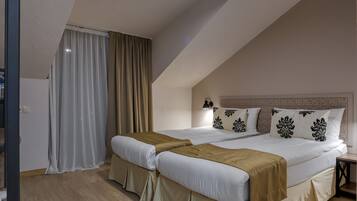 Un dormitorio con dos camas, ropa de cama color beige, piso de madera y una mesita de noche con lámpara.