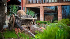 A garden with a wooden cart, a tree, and a building with a balcony in the background. - Savaneti (Telavi)