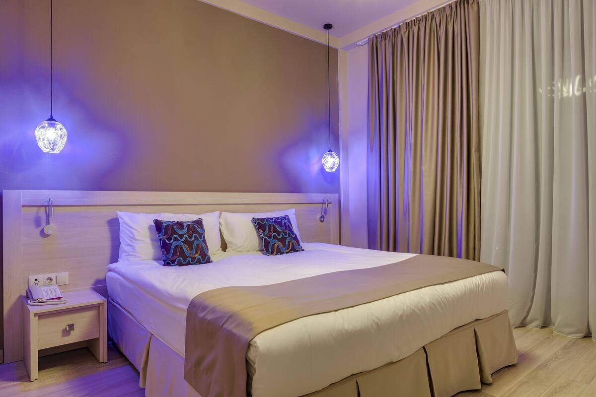 Uma cama bem arrumada com cabeceira, mesa de cabeceira com telefone e bloco de notas, e luminária suspensa.