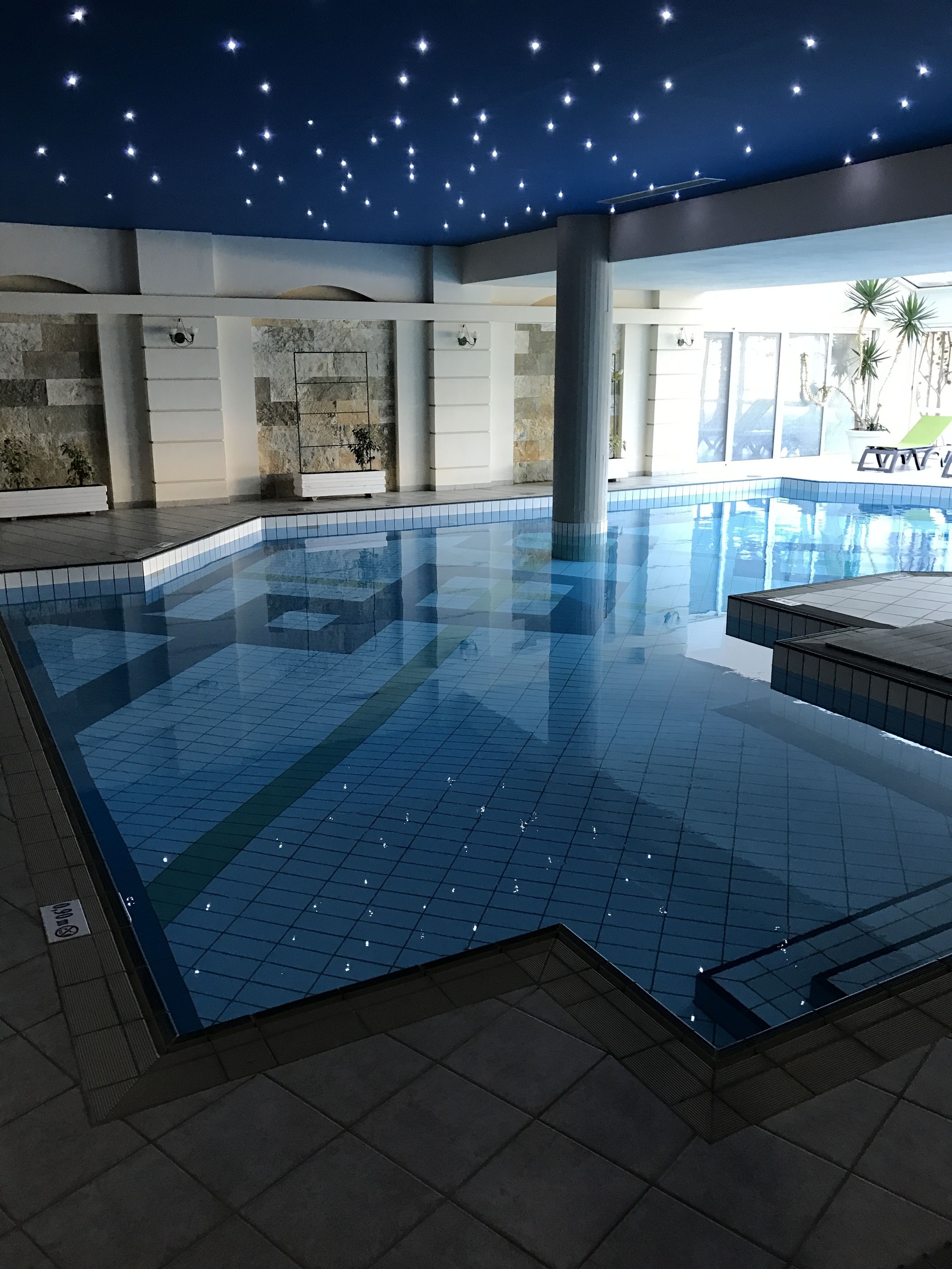 An indoor swimming pool with clear blue water, surrounded by tiled walls and a ceiling with star-like lights.