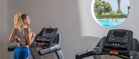 A treadmill with a view of a swimming pool through a window.