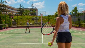 Una cancha de tenis con una red, dos jugadores y un edificio al fondo.