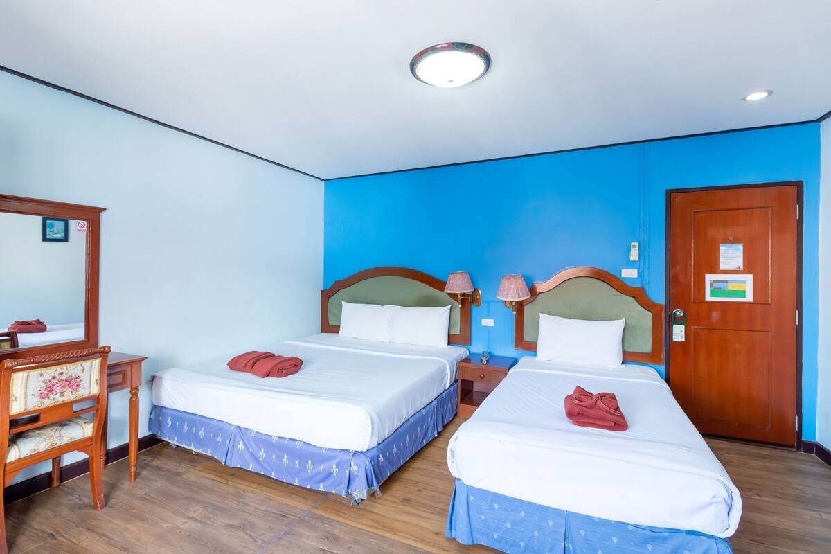 Une chambre d’hôtel avec deux lits, une commode en bois, un miroir et un mur d’accent bleu.