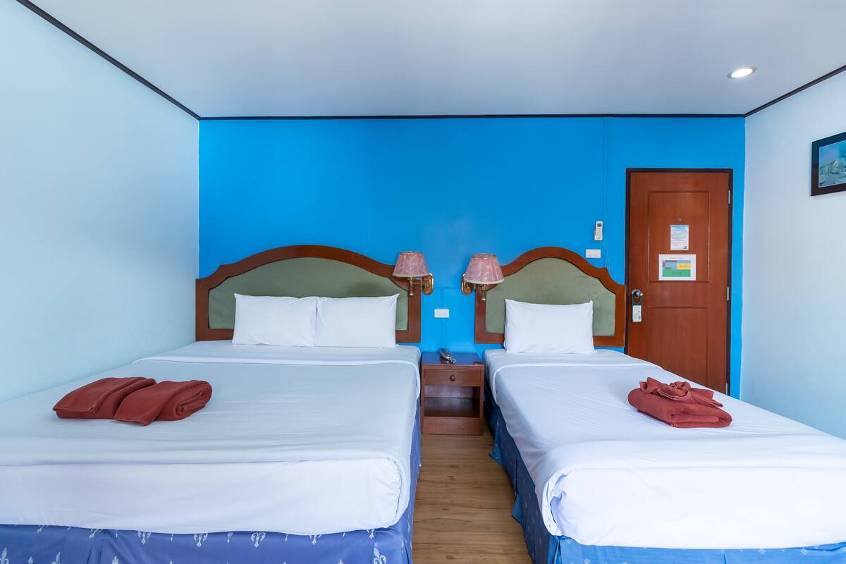 Une chambre d’hôtel avec deux lits, chacun doté d’une tête de lit en bois et de linge de lit blanc. On y trouve deux tables de chevet avec des lampes, ainsi qu’une porte en bois sur laquelle est apposée une pancarte.