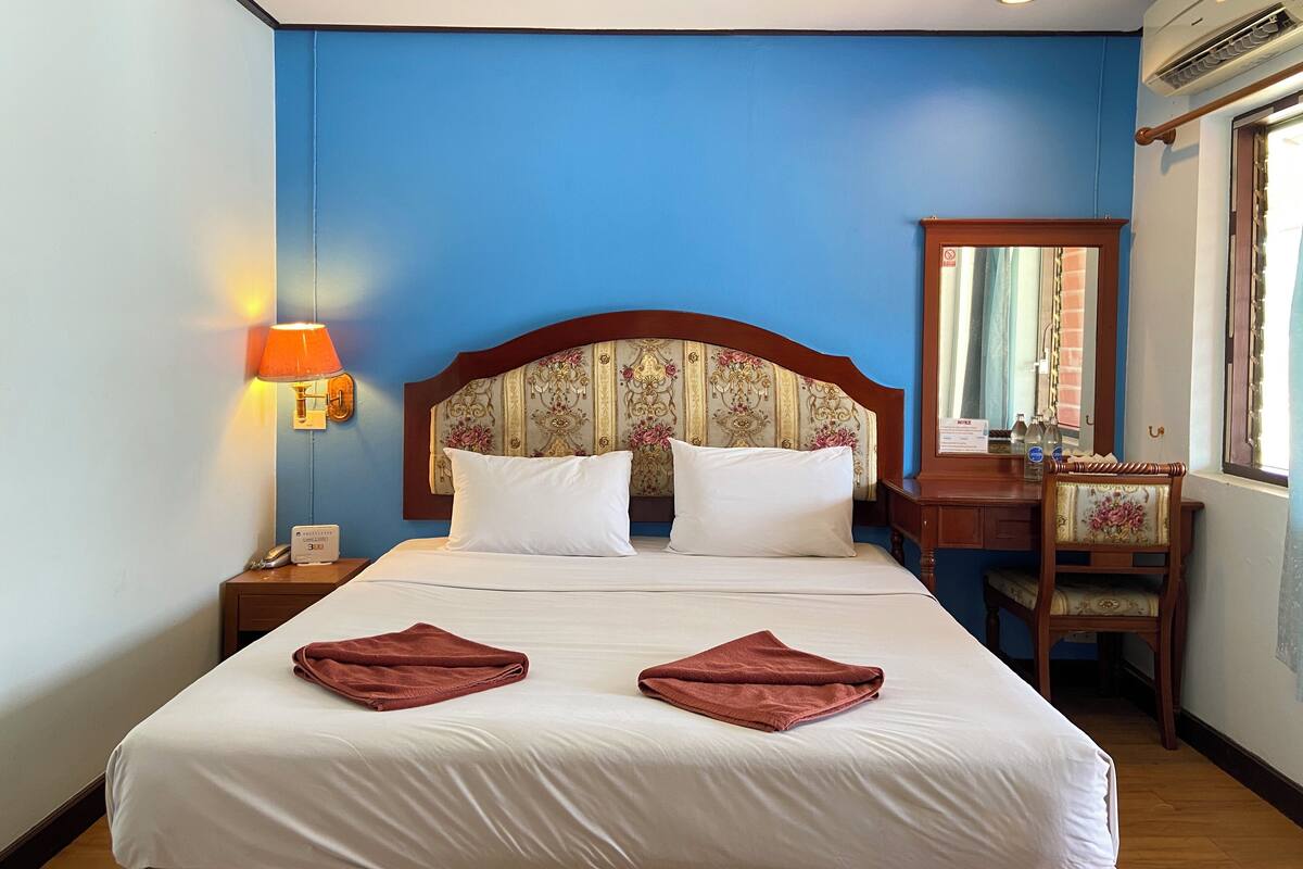 Une chambre d’hôtel avec un grand lit, une table de chevet avec une lampe, un bureau en bois et un miroir.