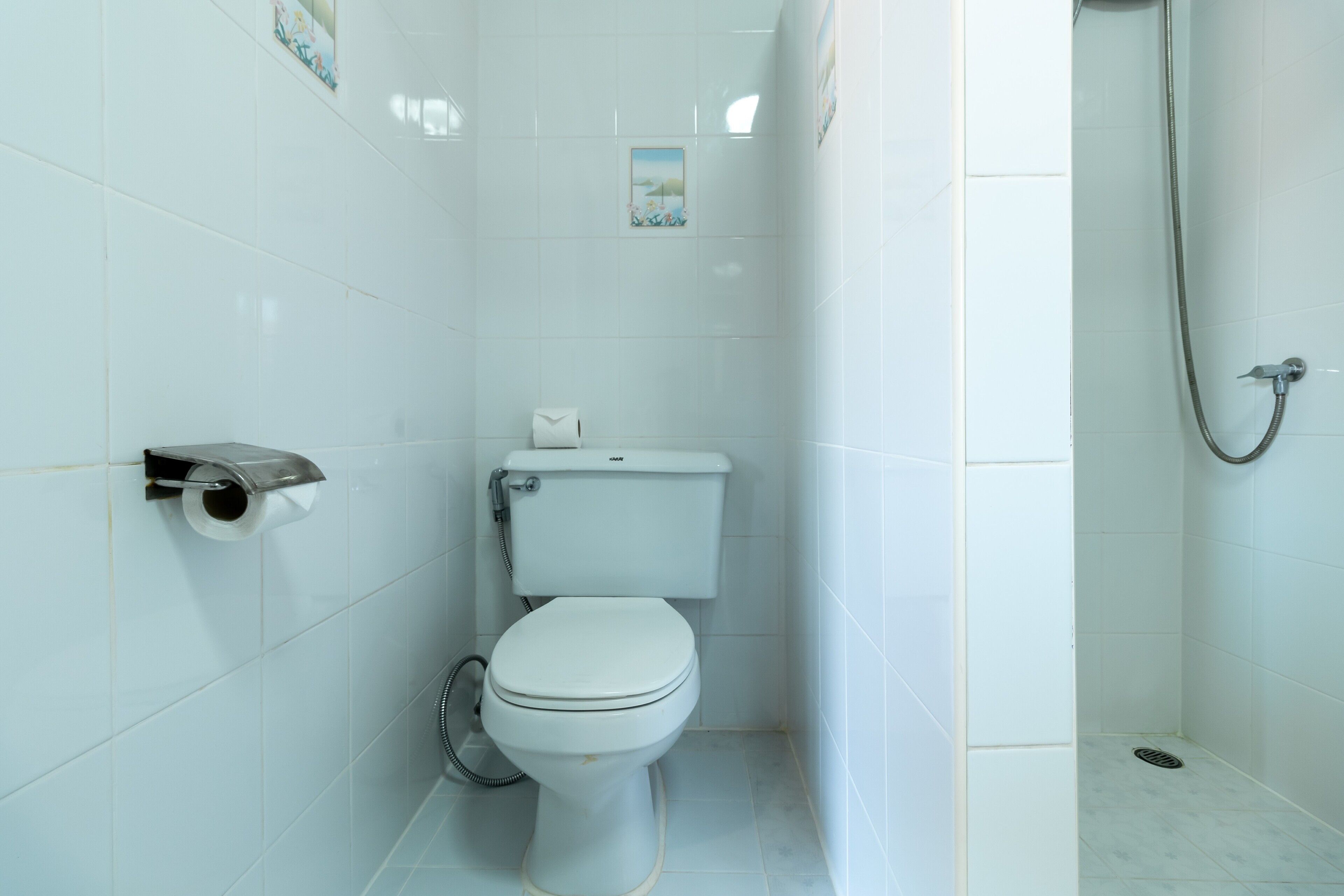 Un baño pequeño y blanco con inodoro, porta papel higiénico y zona de ducha.