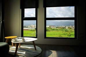 A room with large windows offering a view of a green landscape and distant buildings. There is a round table with two cups and a book.