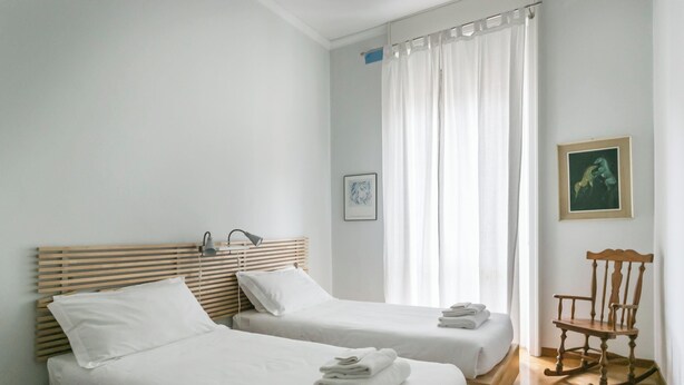 A hotel room with two single beds, a wooden rocking chair, and a large window with curtains. - Italianway   - Da Procida (Milan)