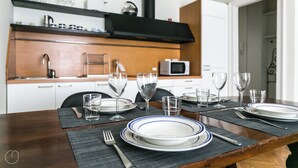 A dining table set with plates, glasses, and cutlery in a modern kitchen with white cabinets and a black range hood. - Italianway   - Da Procida (Milan)