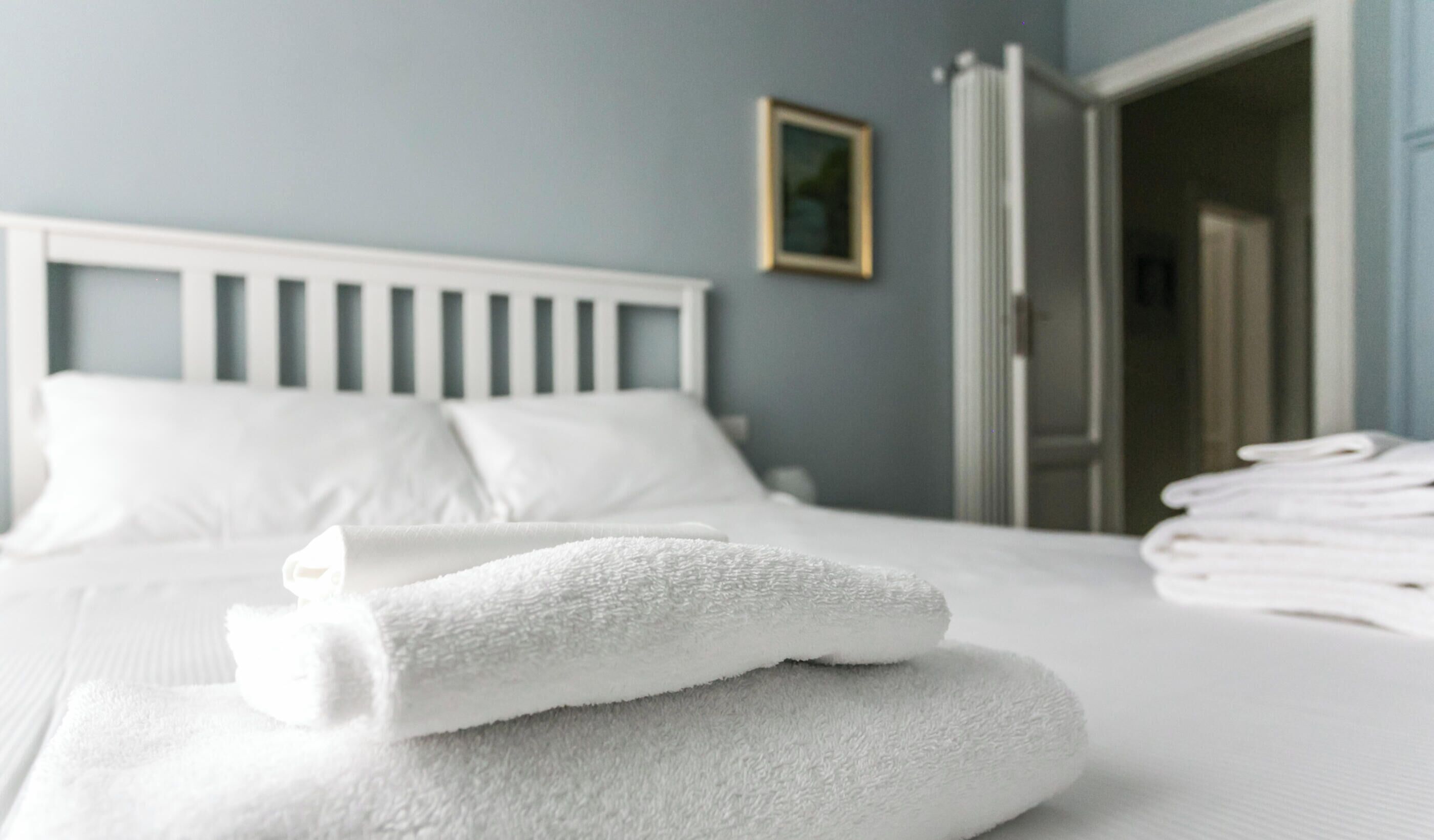 A neatly made bed with white linens and towels, a white headboard, and a framed picture on the wall.