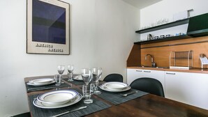 A dining area with a table set for four, a kitchen area with a sink and shelves above, and a framed picture on the wall. - Italianway   - Da Procida (Milan)