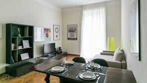 A dining area with a table set for four, a bookshelf, a television, and framed pictures on the walls. - Italianway   - Da Procida (Milan)