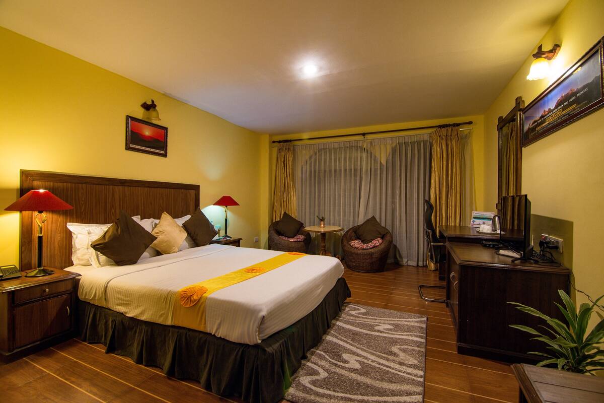 Ein Hotelzimmer mit einem großen Bett, einem Schreibtisch mit Computer, einem Sessel, einem kleinen Tisch und einem Fernseher.