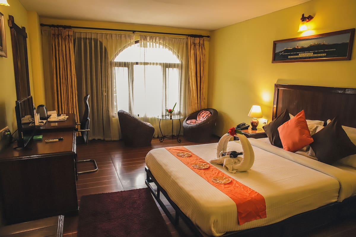 Ein Hotelzimmer mit Bett, Schreibtisch, Stuhl, Nachttisch und einem Fenster mit Vorhängen.