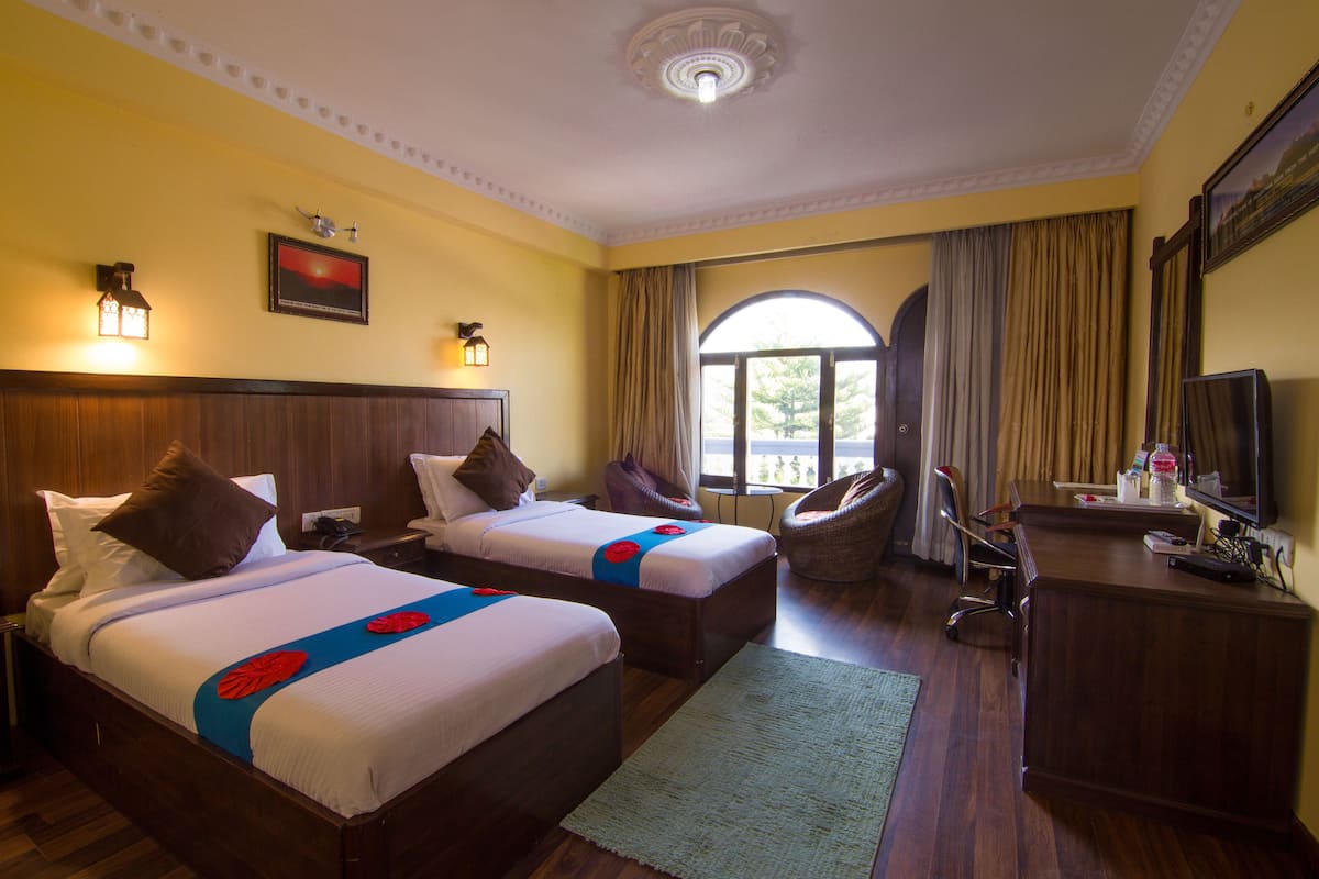 Ein Hotelzimmer mit zwei Betten, einem Schreibtisch, einem Stuhl, einem Fernseher und einem großen Fenster mit Vorhängen.
