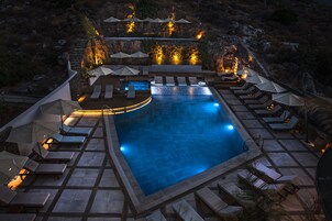 Un área de piscina con sillones de descanso y sombrillas, rodeada de muros de piedra y vegetación.