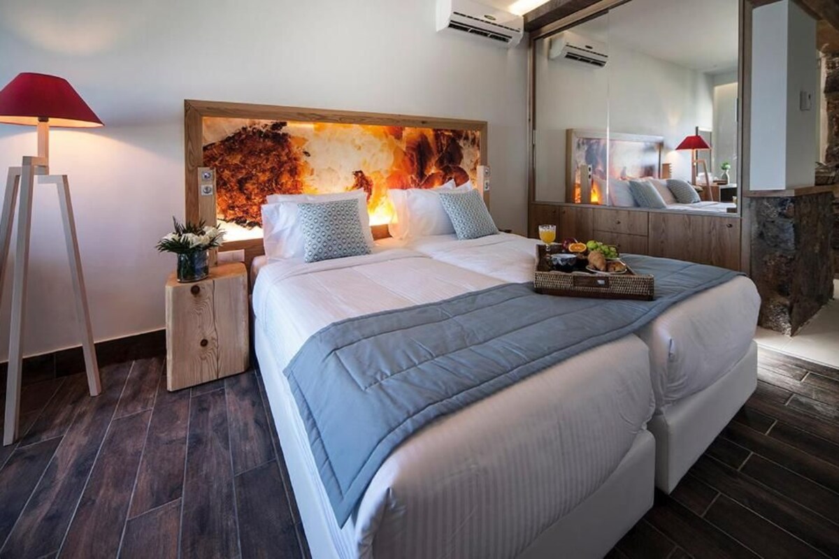 Quarto moderno com uma cama grande, cabeceira de madeira, mesa de cabeceira com luminária e parede de detalhes em pedra.
