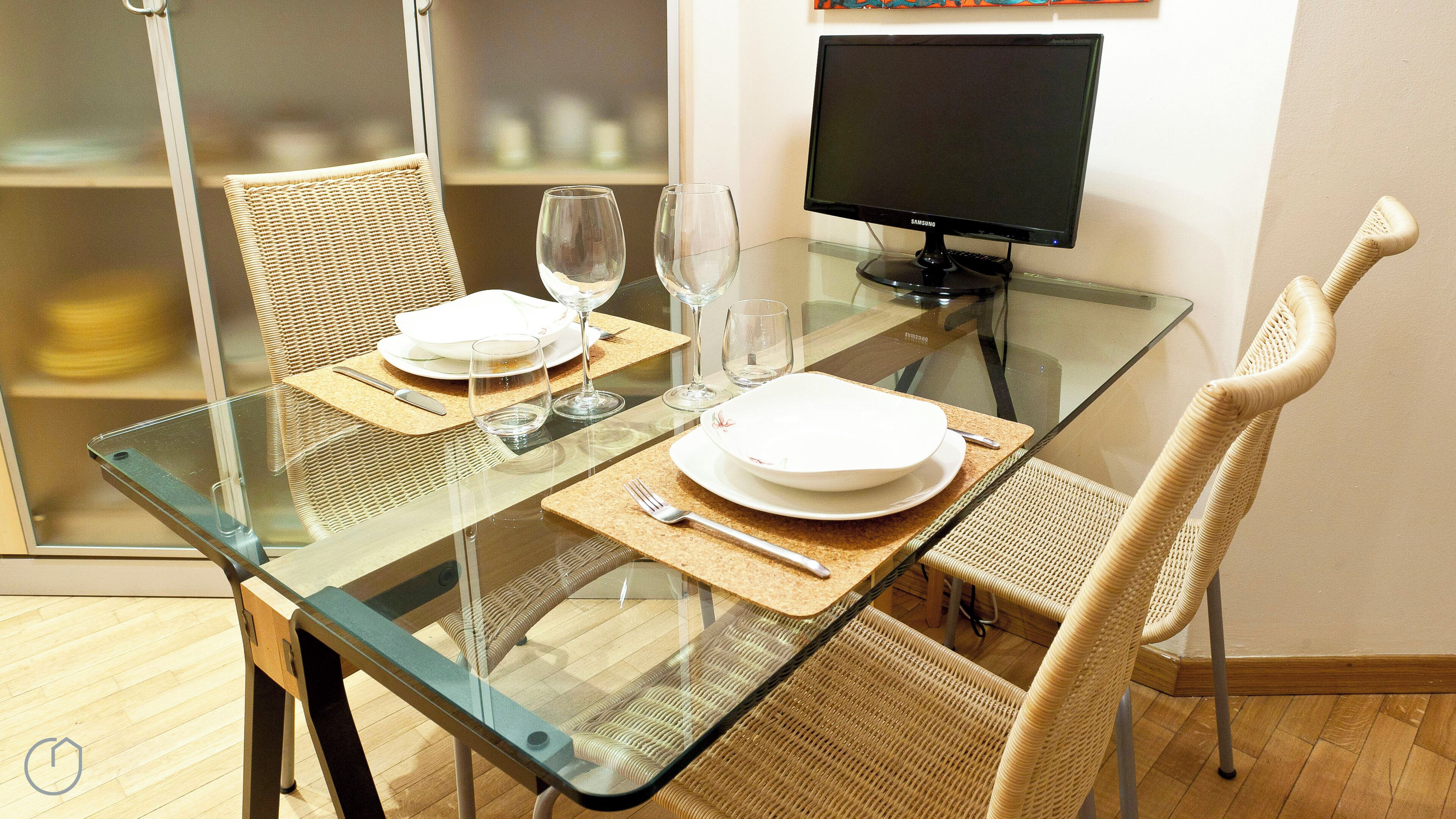 Un coin repas avec une table en verre, des chaises en osier et un téléviseur à écran plat.