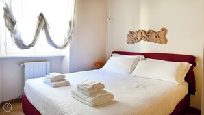 A neatly made bed with white linens and towels, a red headboard, and a wall-mounted artwork. - Italianway - Fiori Chiari (Milan)
