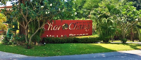 A sign for Chon Ching Villas Resort surrounded by lush greenery and palm trees.