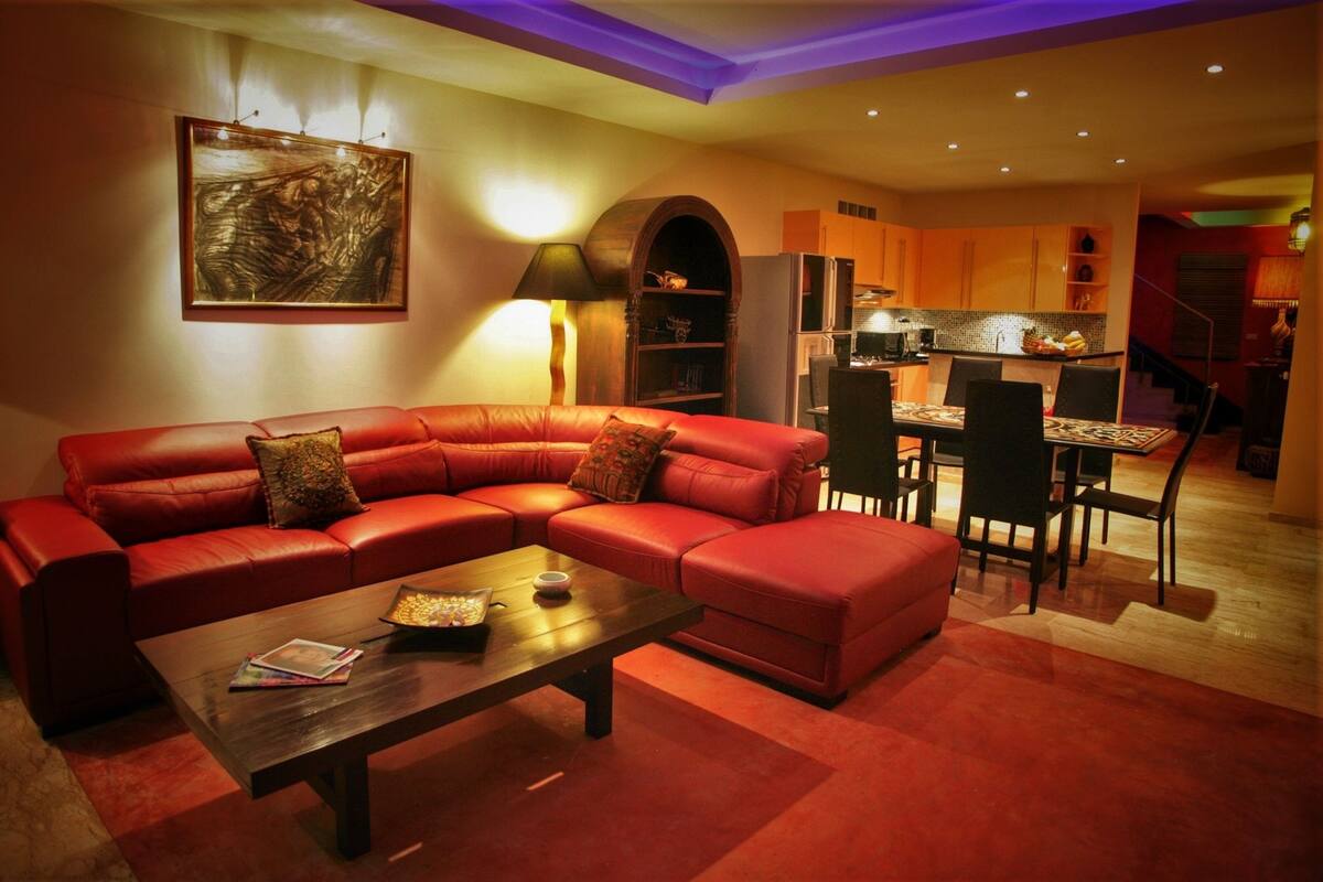 A living room with a red leather sofa, a coffee table, and a dining area with a table and chairs.