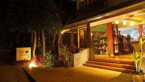 A well-lit hotel entrance with steps leading up to a covered area, surrounded by potted plants and a signboard. - Chor Chang Villa Resort (Koh Samui)