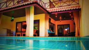 A swimming pool with a tiled edge, a covered outdoor seating area with chairs and tables, and a balcony with railings. - Chor Chang Villa Resort (Koh Samui)