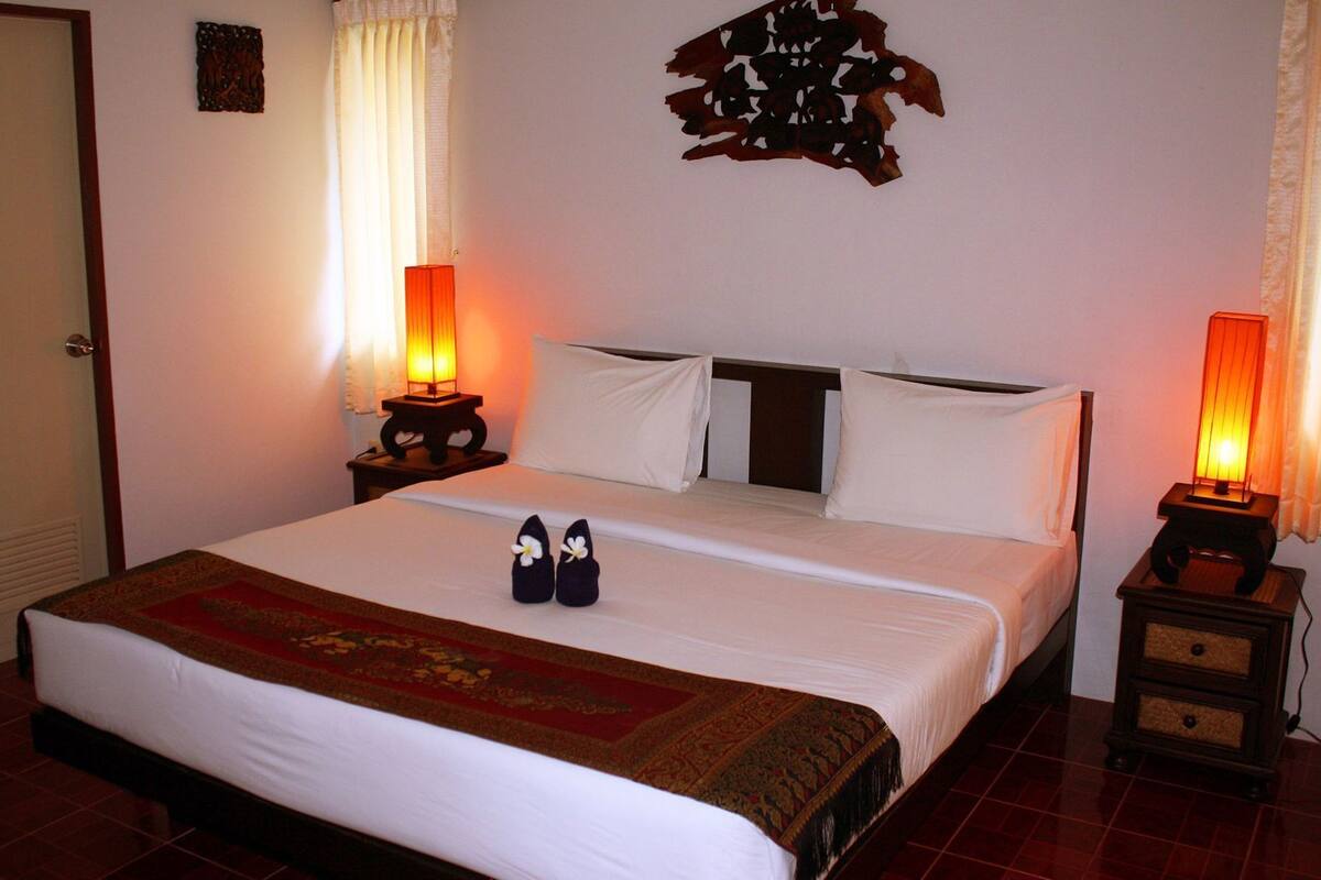 A neatly made bed with a red and gold patterned bedspread, two bedside lamps, and a decorative wall piece.