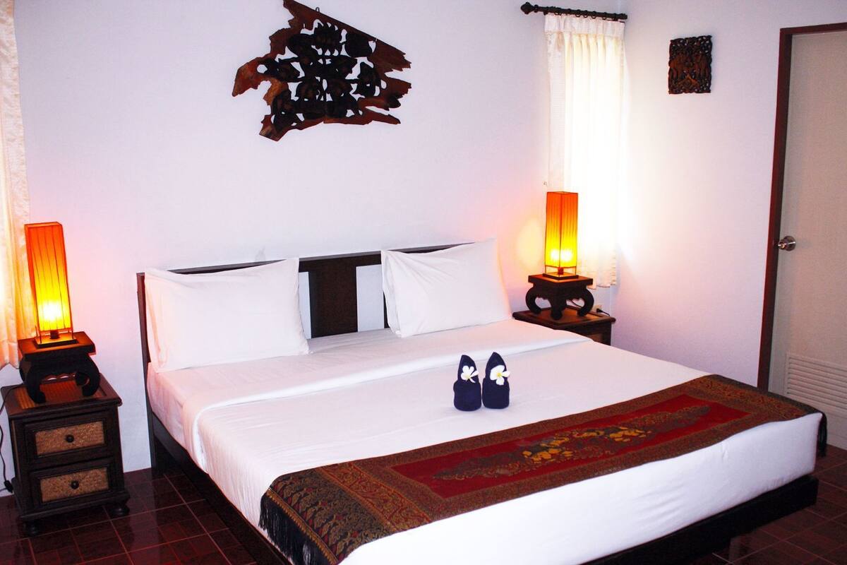 A neatly made bed with white linens, two bedside lamps, a decorative wall piece, and a pair of shoes on the bed.