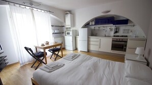 Una habitación de hotel compacta con cama, un escritorio pequeño, una silla, kitchenette y baño.