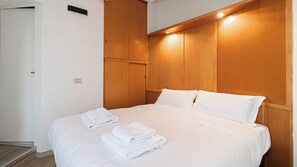 A hotel room with a wooden headboard, a bed with white linens, and two folded towels on the bed.