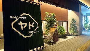 A building entrance with a sign in Japanese, a small garden with plants and a rock, and a paved walkway. - Cabinhouse Yado Fujinomiyaten (Fujinomiya)