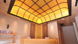A reception area with a wooden reception desk, a curved ceiling with recessed lighting, and a wall-mounted shelf with framed pictures. - Cabinhouse Yado Fujinomiyaten (Fujinomiya)