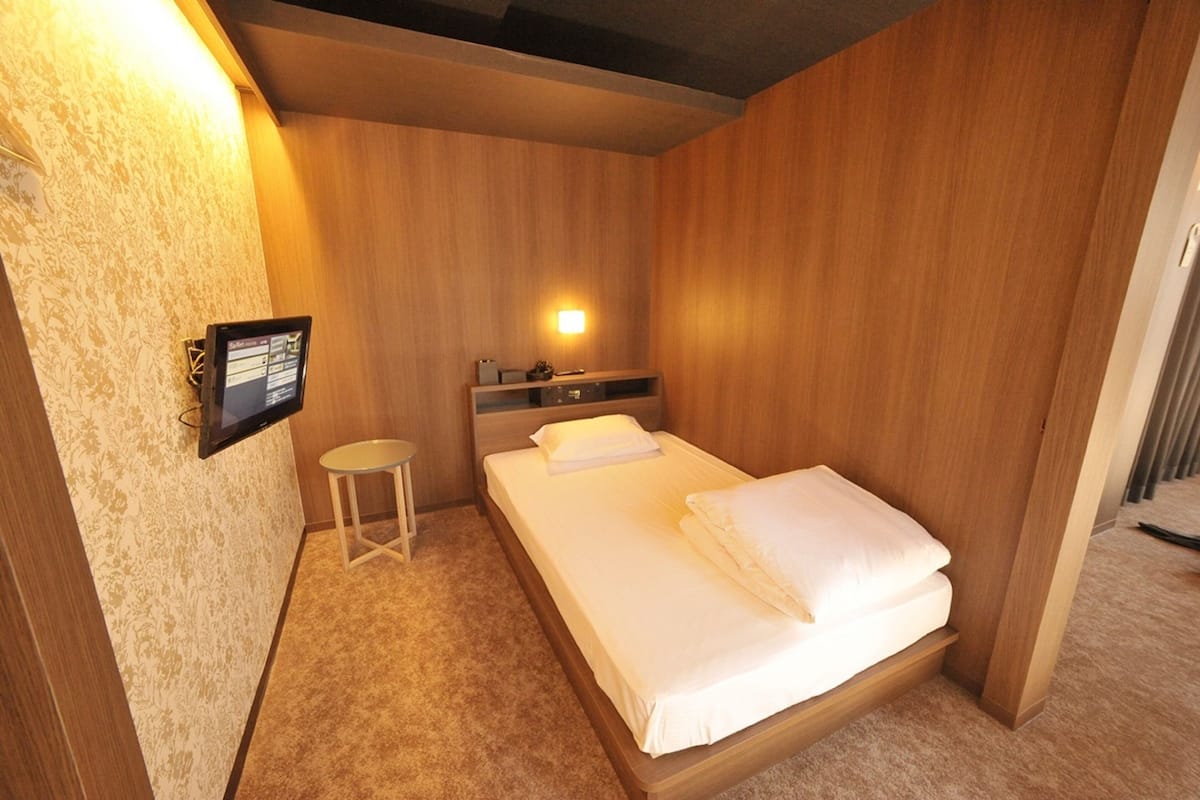 A hotel room with a wooden wall, a bed with white linens, a small round table, and a wall-mounted TV.