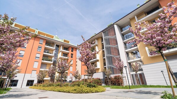 A modern apartment building with balconies, a central courtyard, and flowering trees.