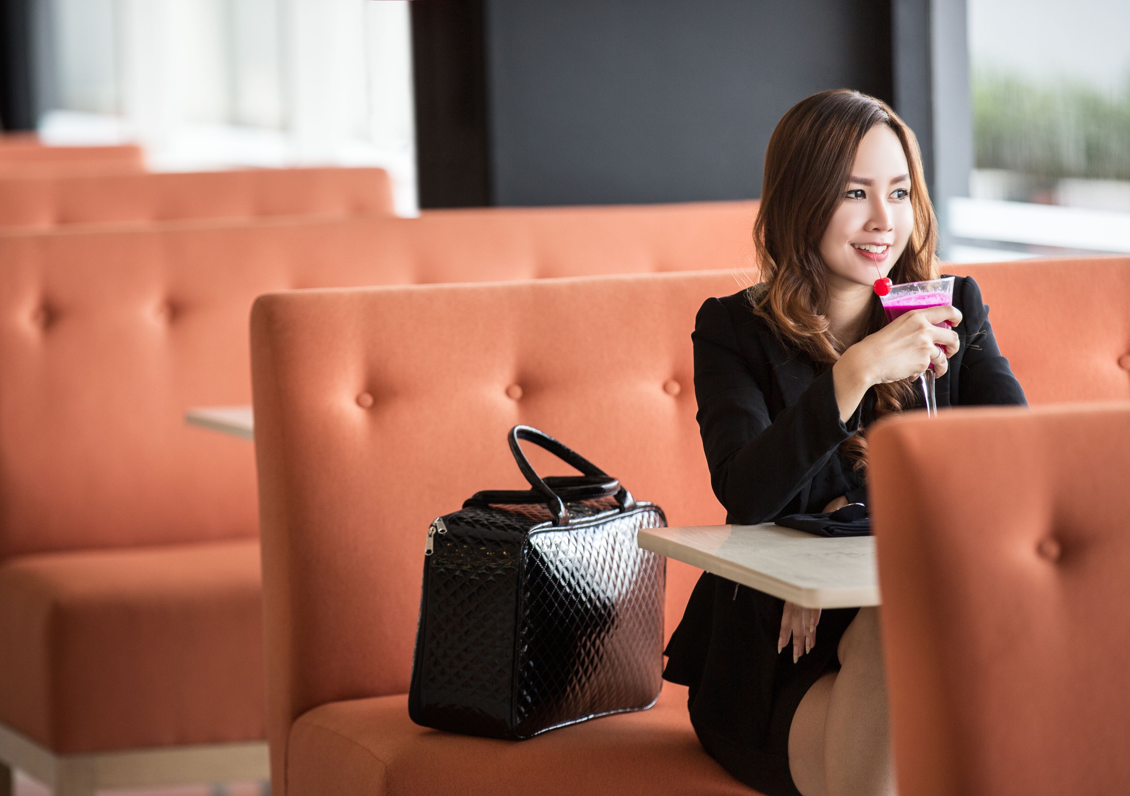 A person seated on an orange cushioned bench with a black handbag beside them.