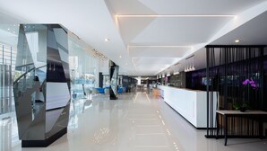 A modern hotel lobby with a glass facade, a reception desk, and a seating area with blue chairs. - INNSiDE by Meliá Yogyakarta (Depok)