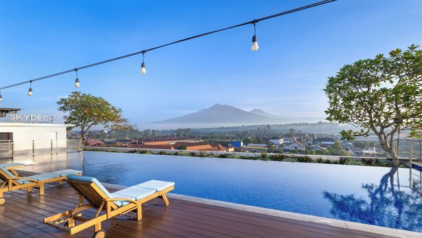 An infinity pool with wooden deck and lounge chairs, overlooking a mountain and a town. - INNSiDE by Meliá Yogyakarta (Depok)