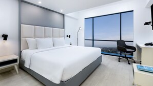 A modern hotel room with a large bed, a desk, and a view of the city through large windows. - INNSiDE by Meliá Yogyakarta (Depok)