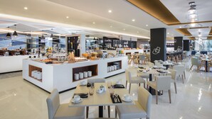 A modern cafe with a central counter displaying food and beverages, surrounded by tables and chairs. - INNSiDE by Meliá Yogyakarta (Depok)