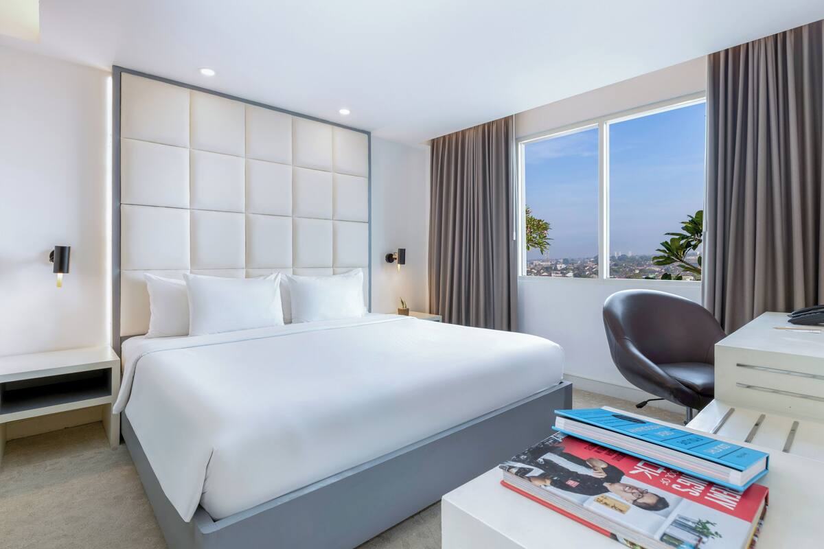 Une chambre d’hôtel moderne, dotée d’un grand lit, d’un bureau et offrant une vue sur la ville.